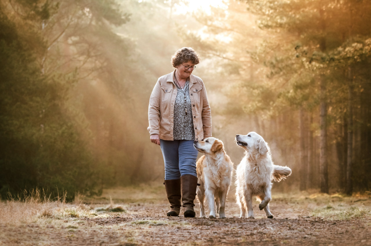 Frau geht mit ihren beiden Hunden im Wald spazieren