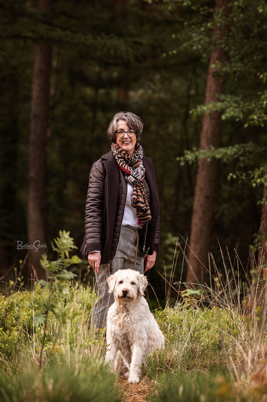 Frau steht im Wald neben ihrem Hund