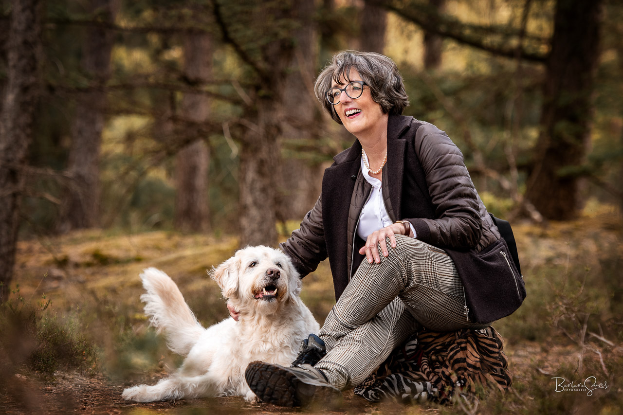 Frau sitzt mit ihrem Hund im Wald