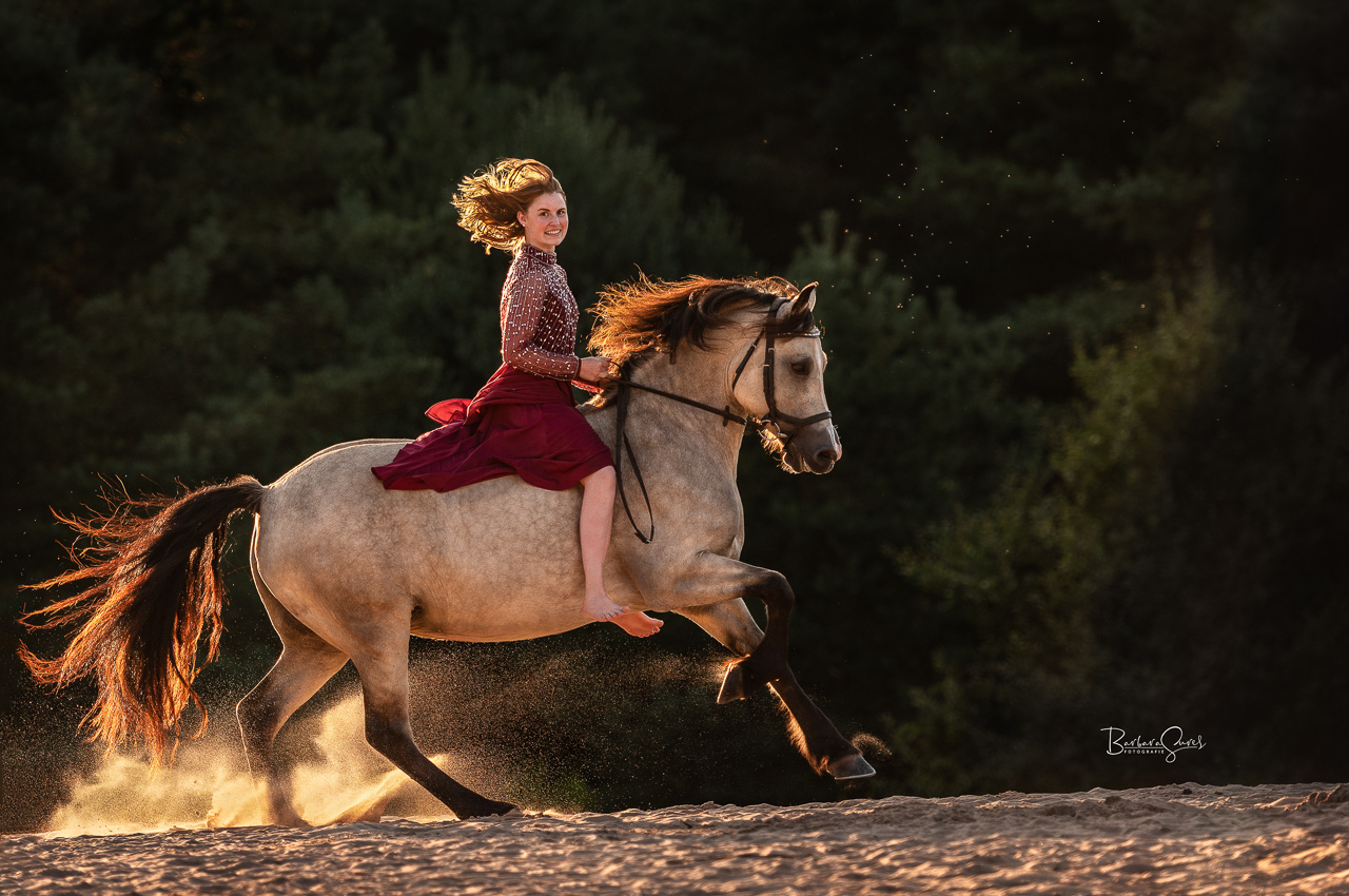 Frau reitet auf ihrem Pferd über den Sand