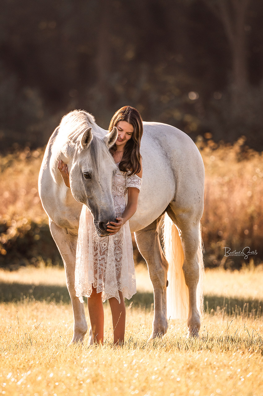 Eine junge Frau steht mit ihrem Pferd auf der Wiese und nimmt es in den Arm