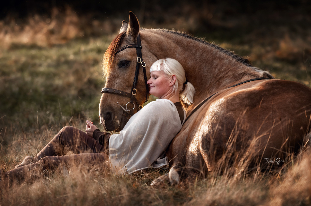 Frau liegt mit Pferd im Gras