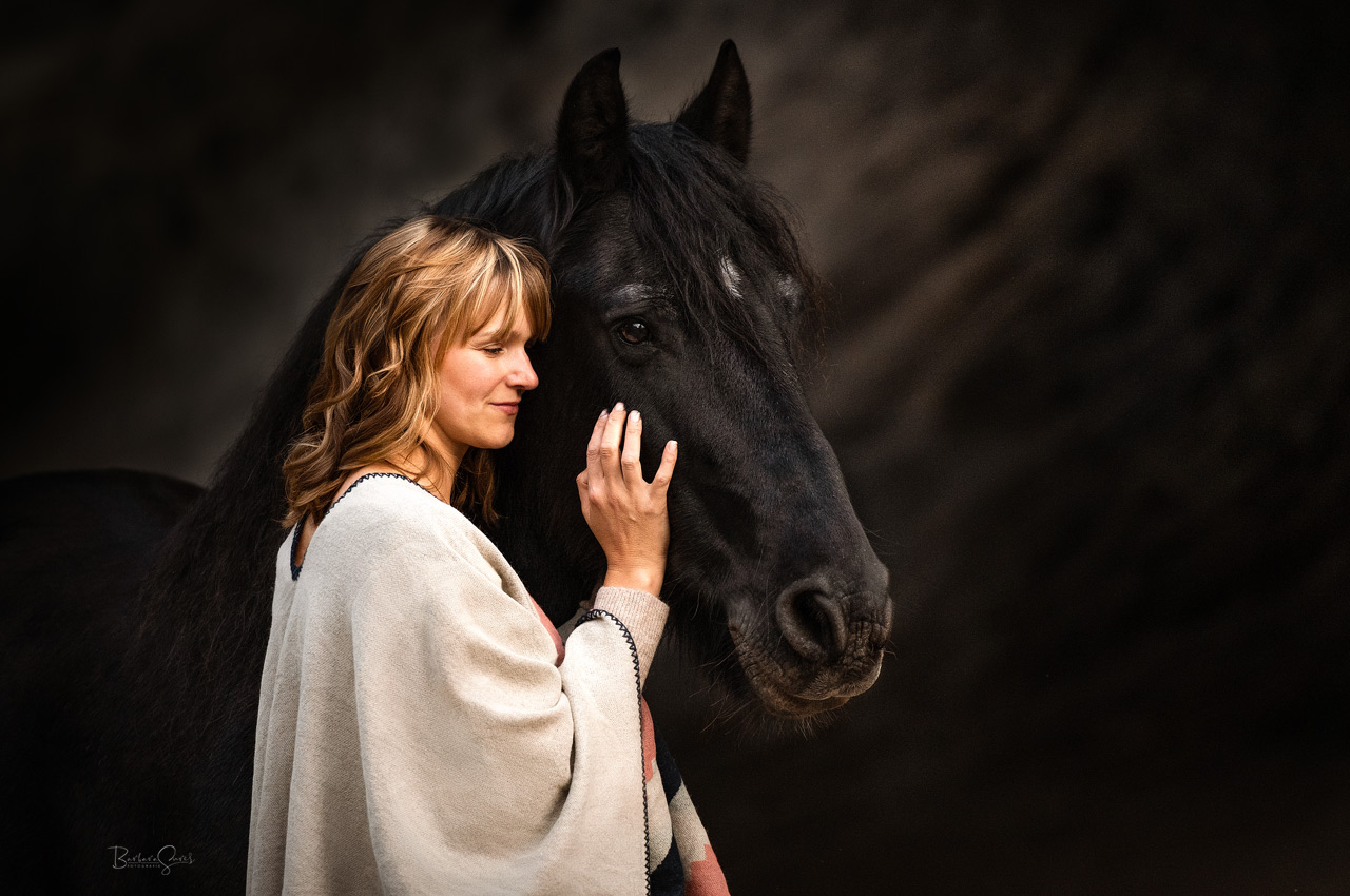 Eine junge, hübsche Frau steht an der Seite ihres schwarzen Pferdes