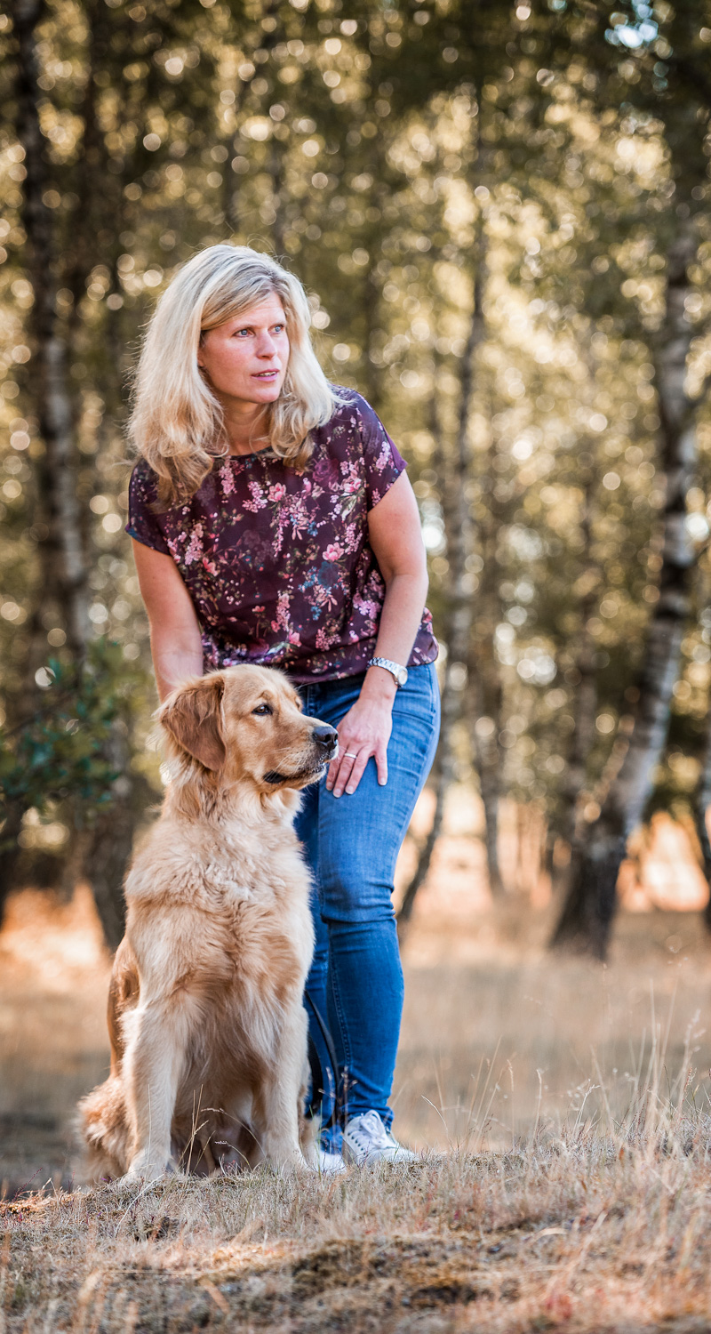 Frau steht mit ihrem Hund auf einer Wiese und streichelt ihn am Kopf